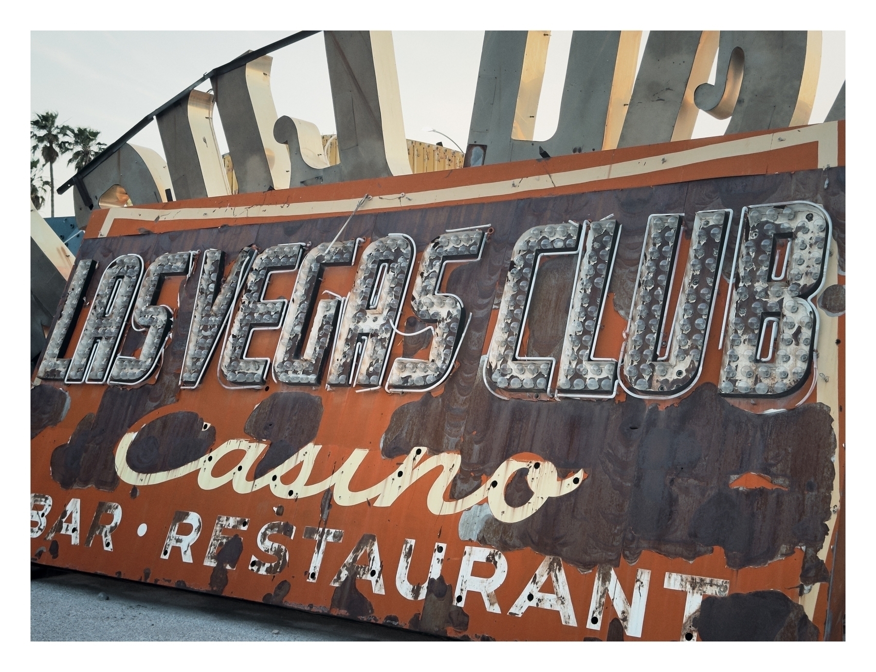 A weathered sign reads “LAS VEGAS CLUB Casino Bar Restaurant,” showcasing faded and rusted letters against a decaying background, evoking nostalgia.