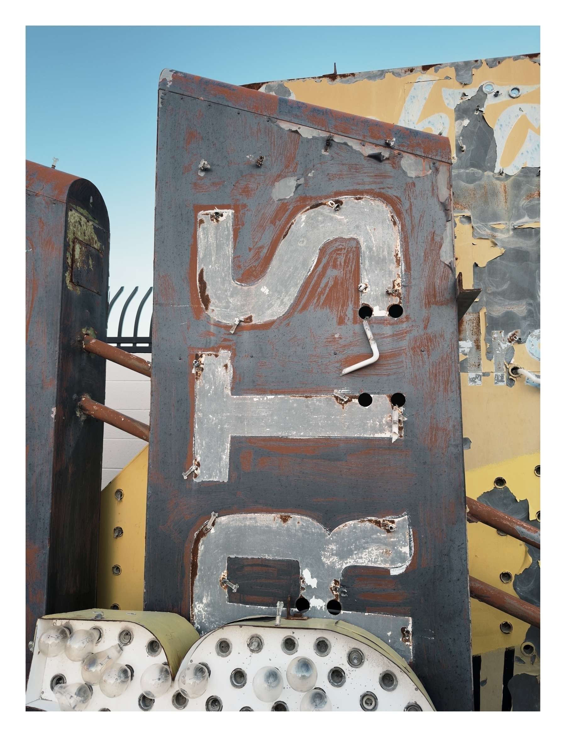 Aged and weathered signage parts, with peeling paint and rust, are stacked against a clear sky.