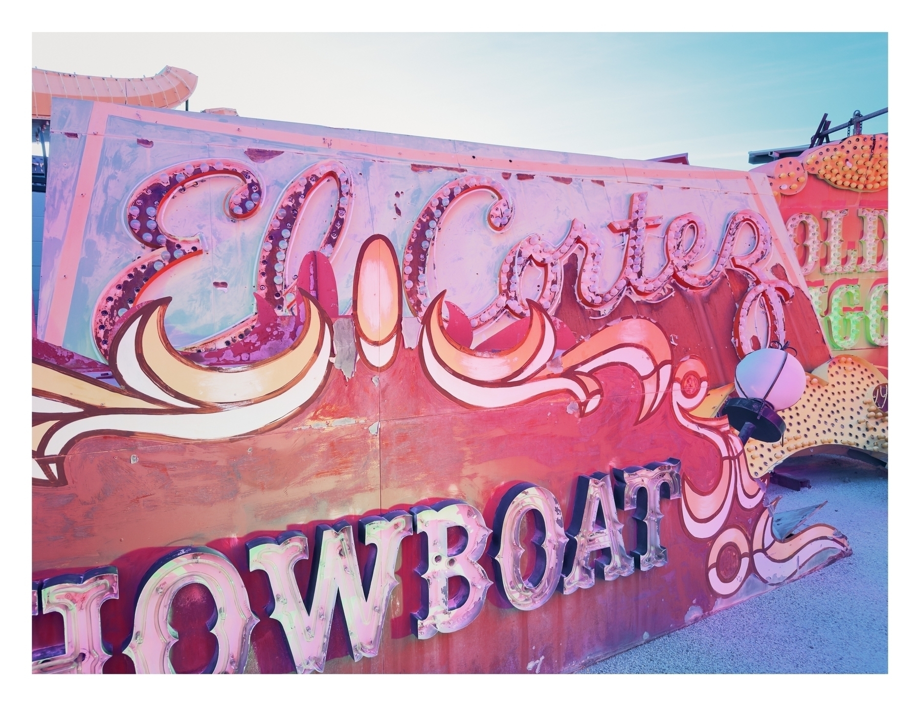 A weathered neon sign reads “El Cortes SHOWBOAT” against a clear sky, suggestive of a vintage establishment or a scrapyard of old signage.