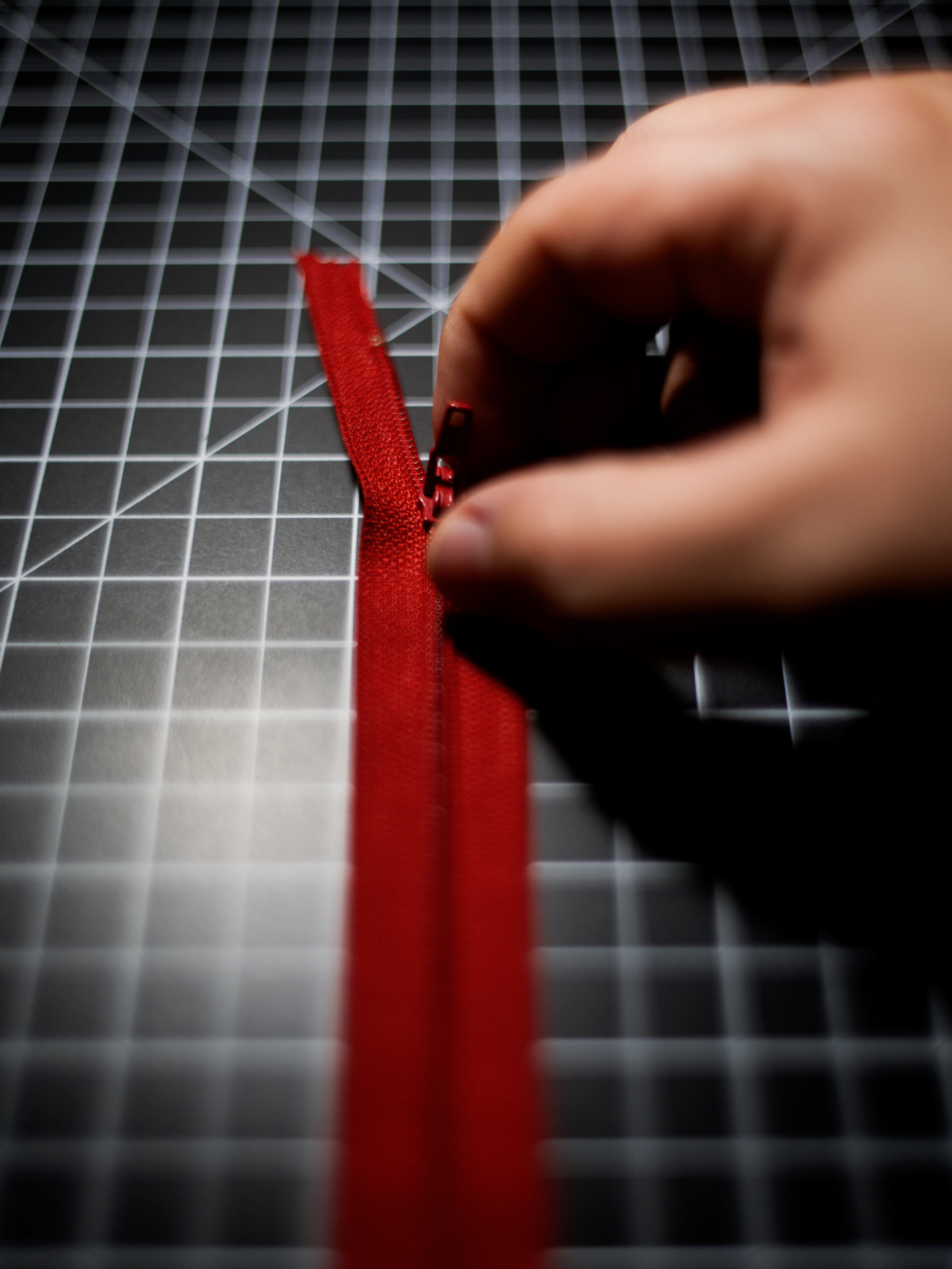 A red zipper being unzipped by a hand above a black and white grid