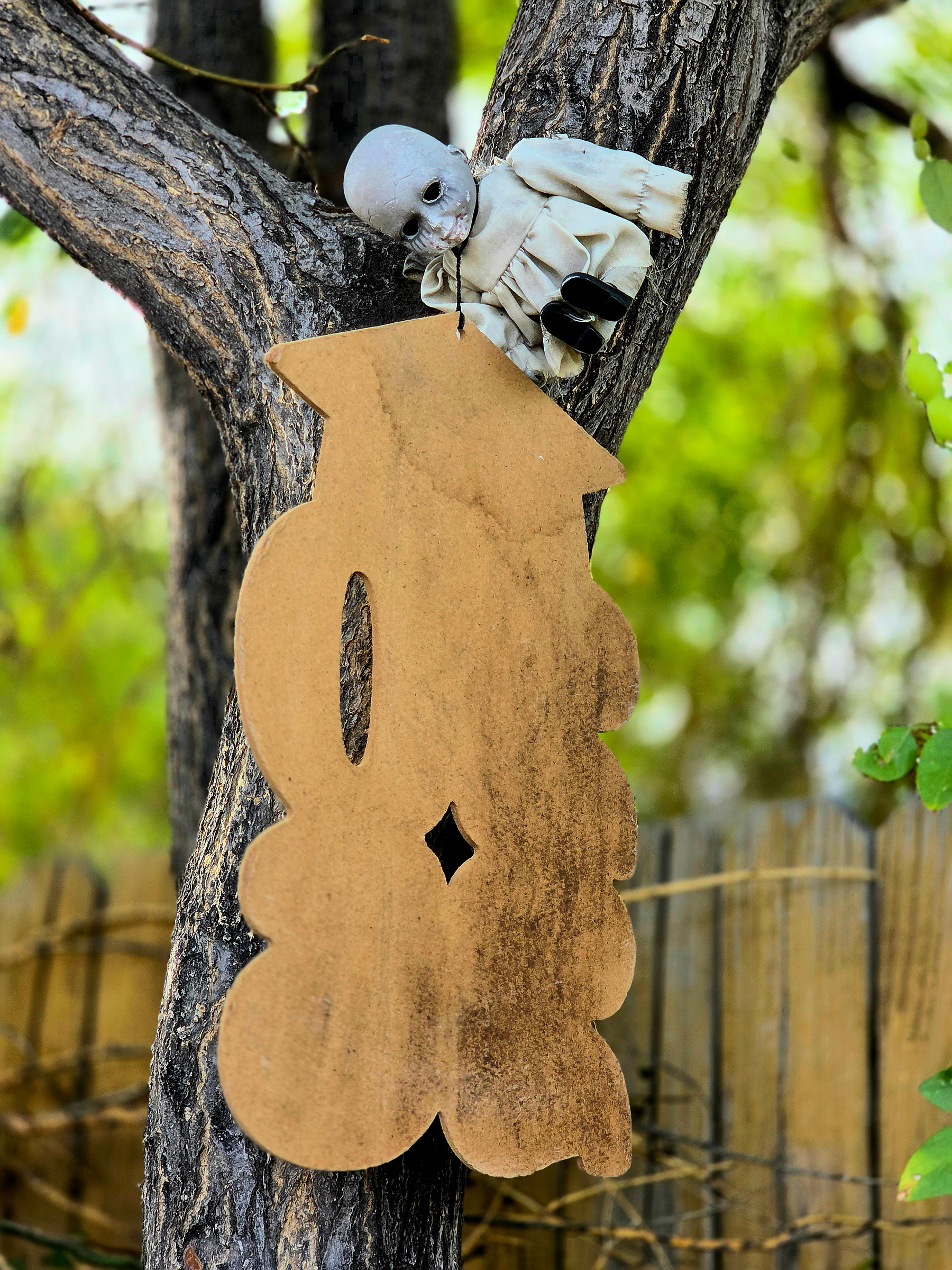 A small doll figure and a decorative sign hanging in a tree