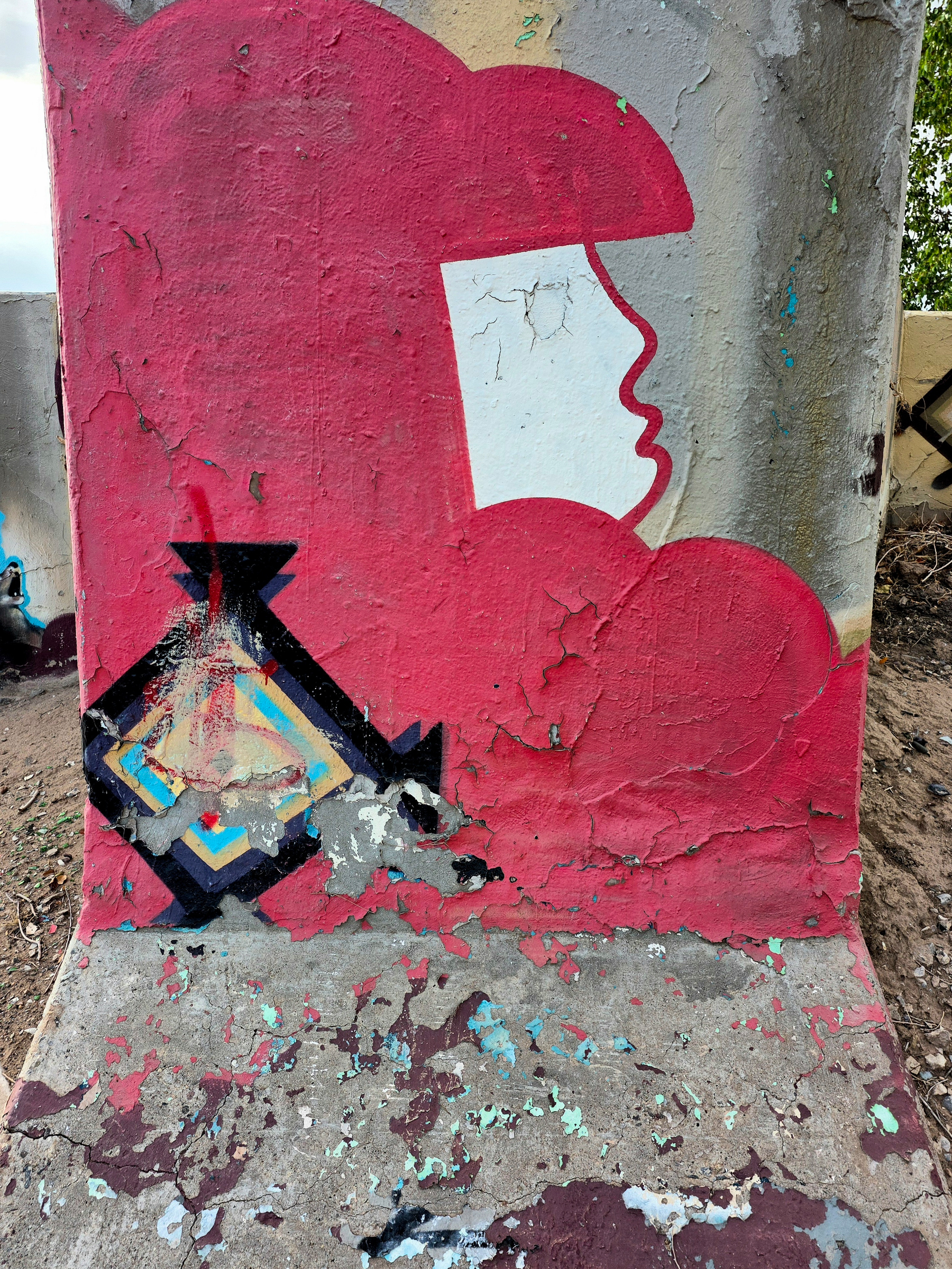 A weathered mural on a concrete pillar with a red cloud shape and painted profile