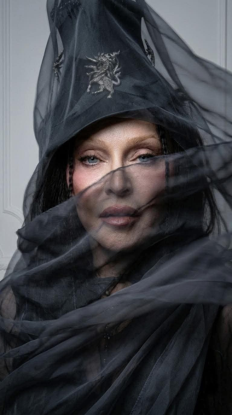 Auto-generated description: A person is partially obscured by flowing, sheer black fabric and wearing a dark, intricate headdress.