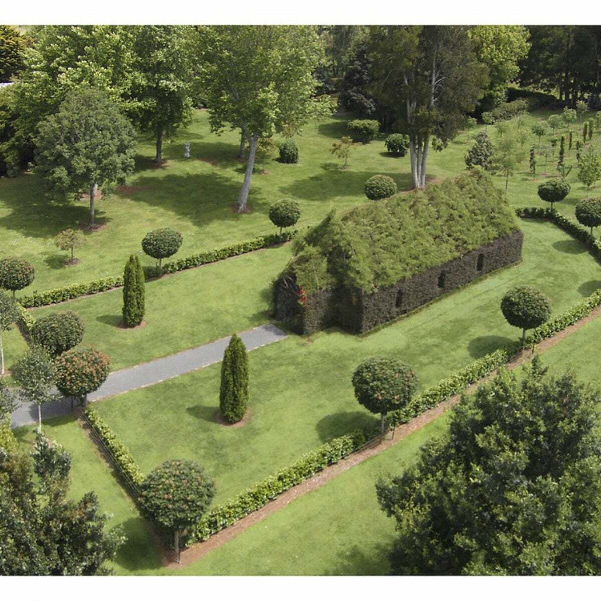Auto-generated description: A lush garden features a small, church-like structure made entirely of greenery and surrounded by neatly trimmed hedges and trees.