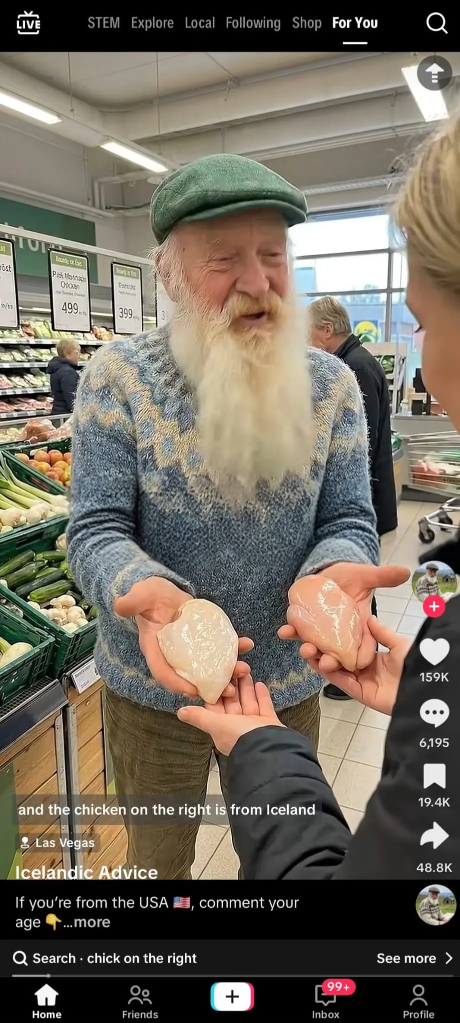 Auto-generated description: An elderly man with a long beard and green cap is holding two pieces of wrapped chicken in a grocery store, engaging with a person standing in front of him.
