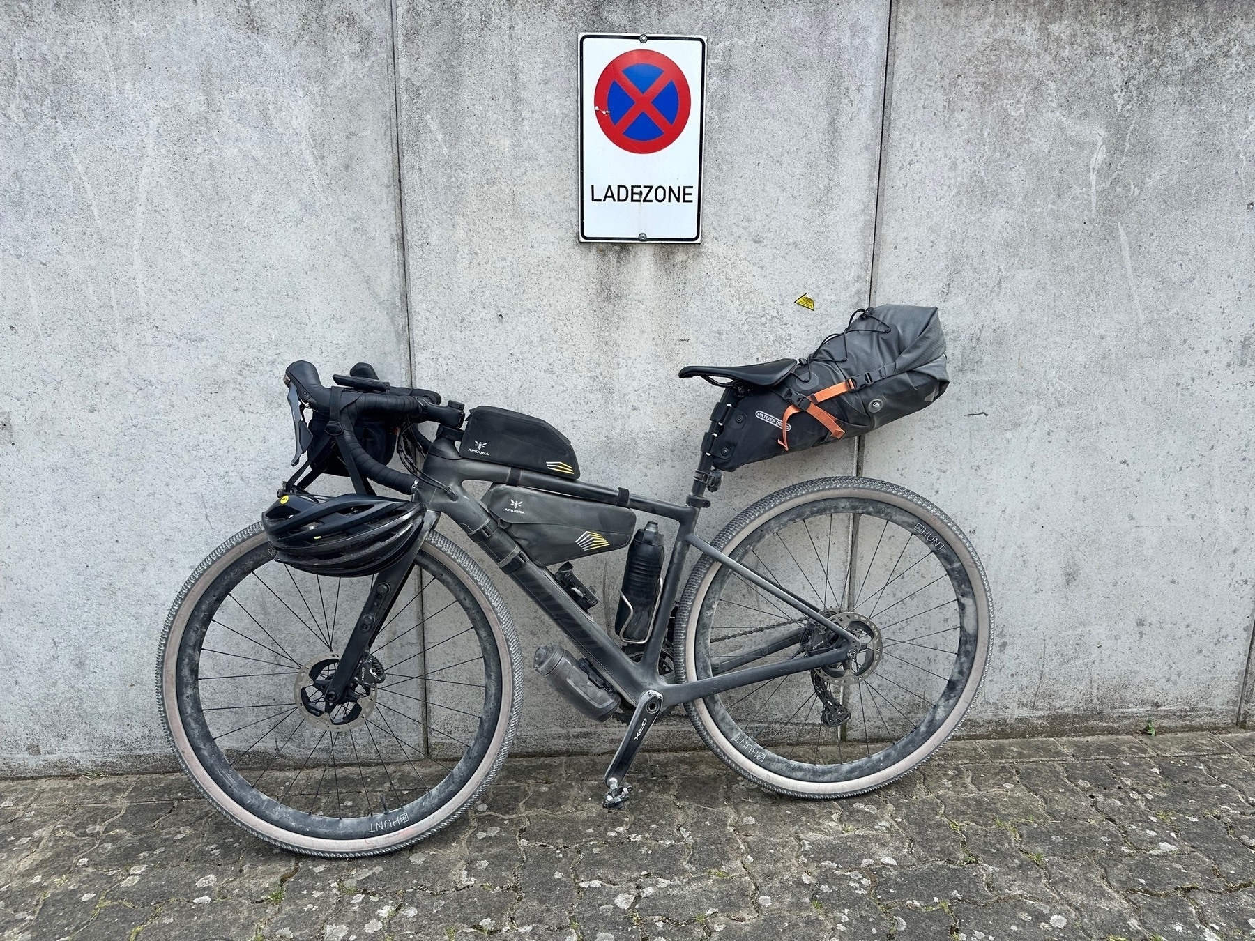 Dusty gravel bike leaning against a concrete wall in front of "loading zone" sign.