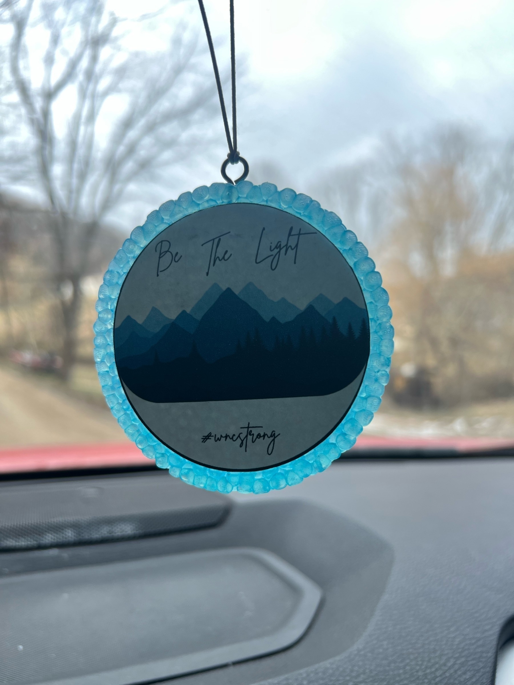 circle with mountains on it hanging from car mirror