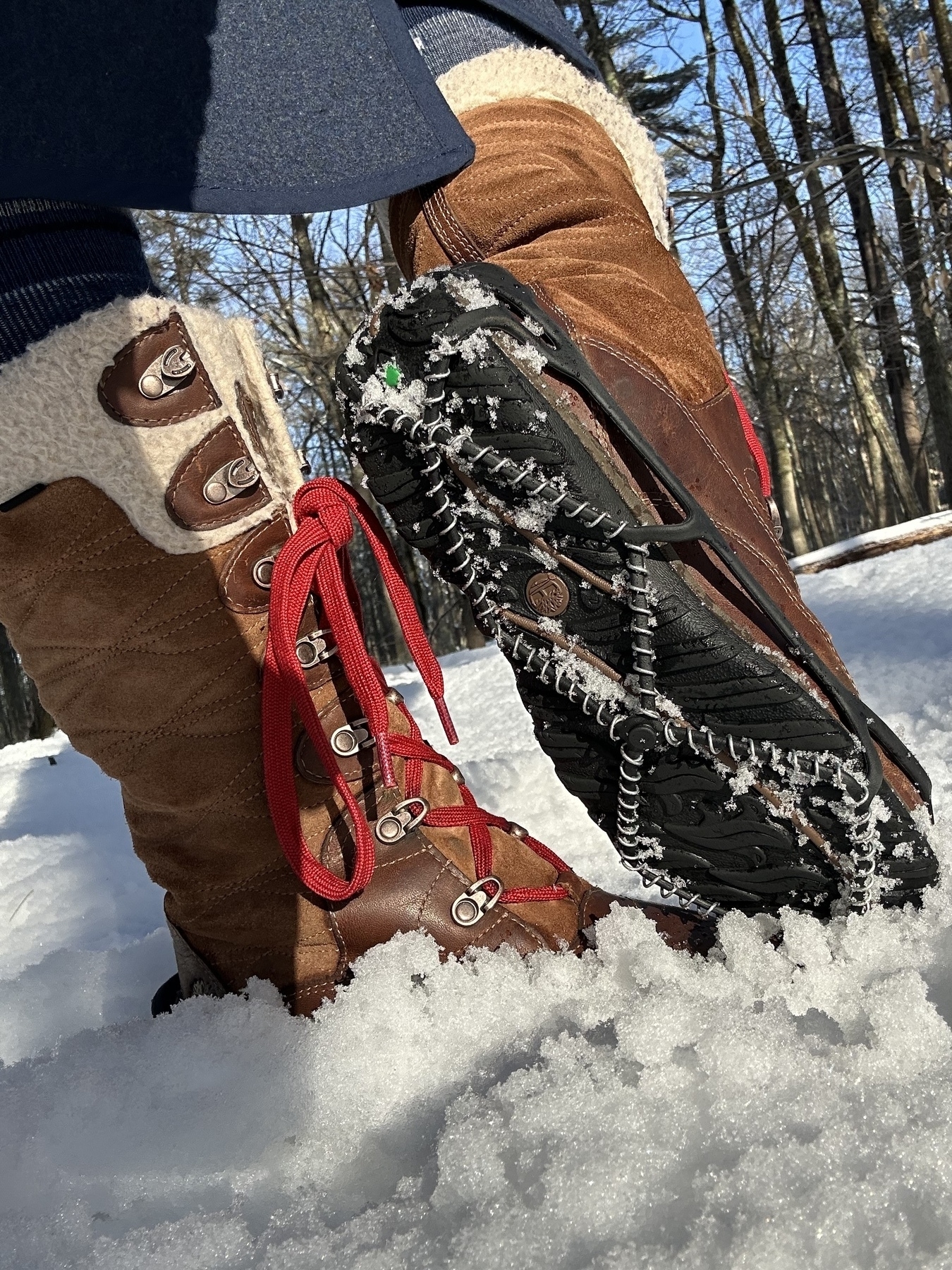 A pair of snow boots in the snow, with Yak Trax on for greater traction while walking on ice