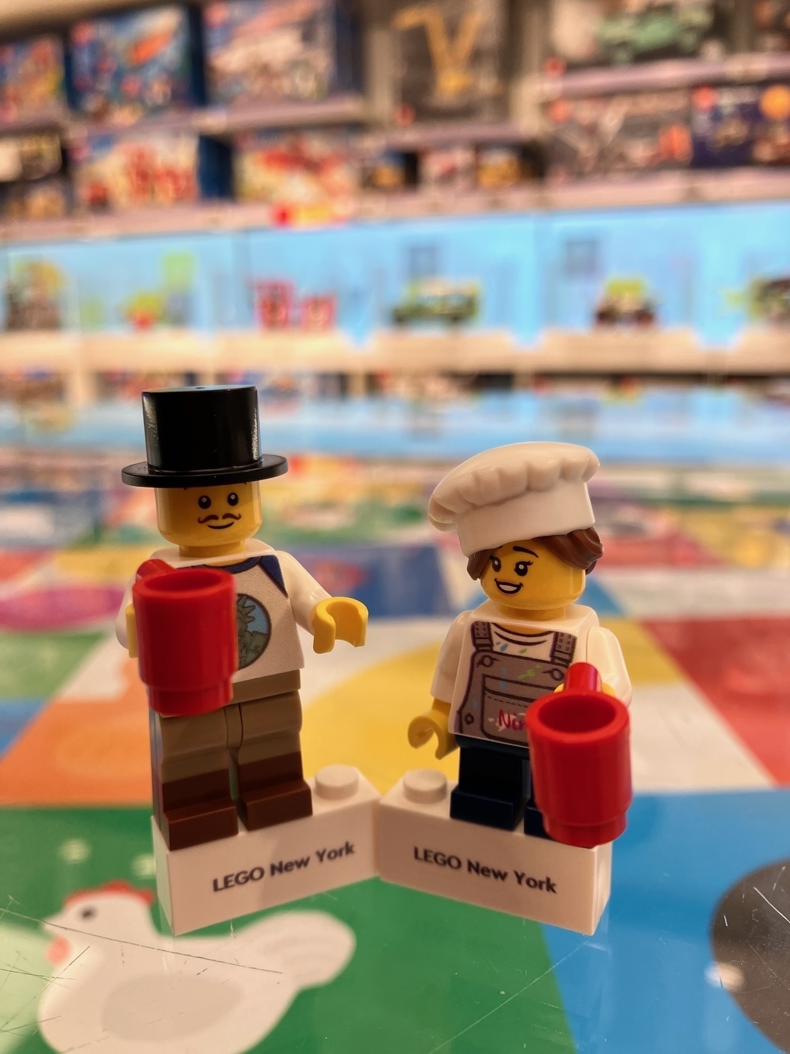 Close up of two Lego figurines. The left one is a man and he has a top hat and a red coffee cup in his hand. The right one is a woman and she has a chefs hat and a red coffee cup in her hand. 