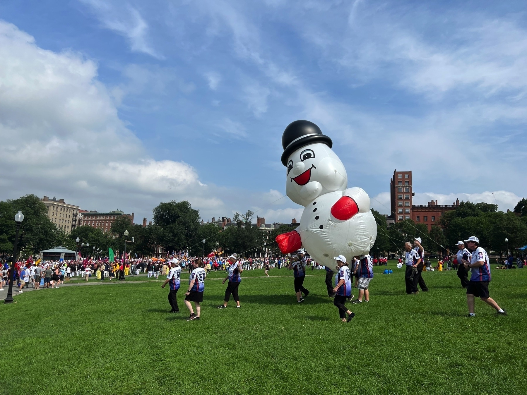 A view of Boston Common. A group of people in the foreground are holding down a large inflatable snowman balloon, part of a Lions Club parade.