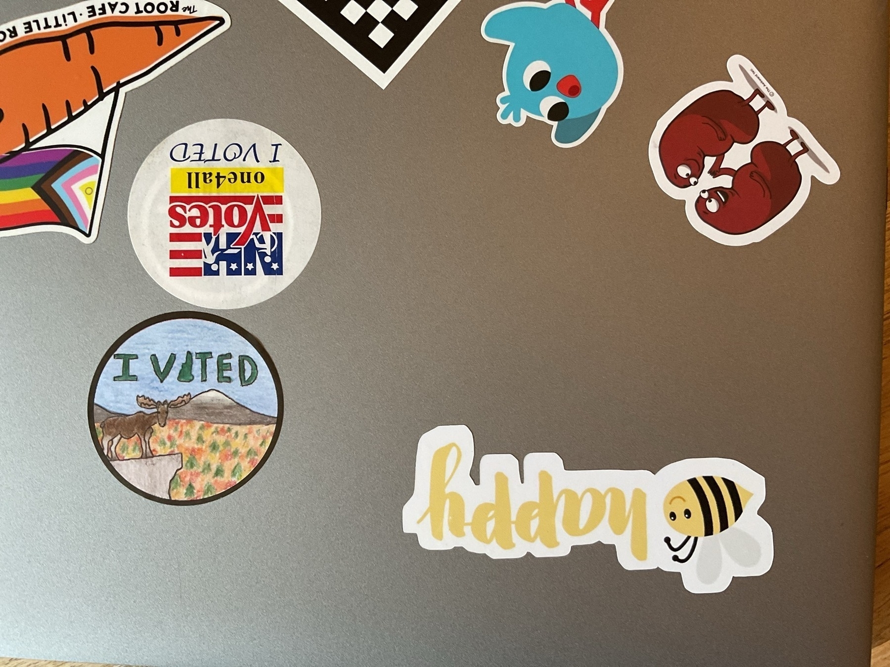 A picture of a metal computer laptop with various stickers on it including the childlike moose illustration and "I Voted" slogan