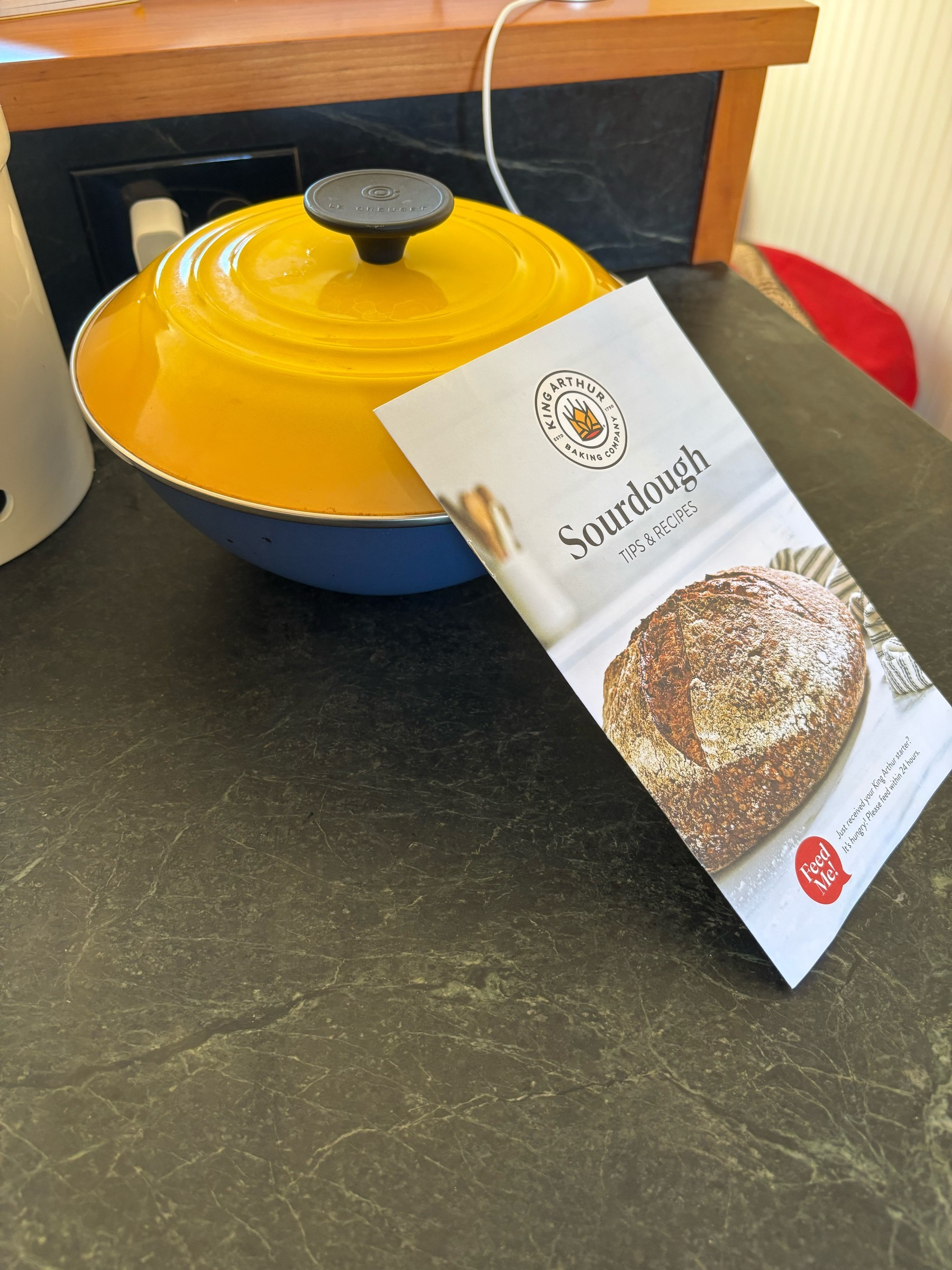 A bright yellow lid on a blue bowl with King's Arthur's sourdough tips and tricks booklet leaning against it