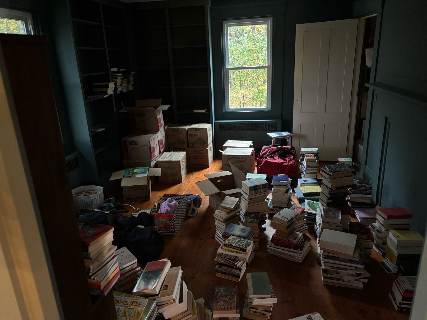 A room full of piles of books, with built in shelves in the background.