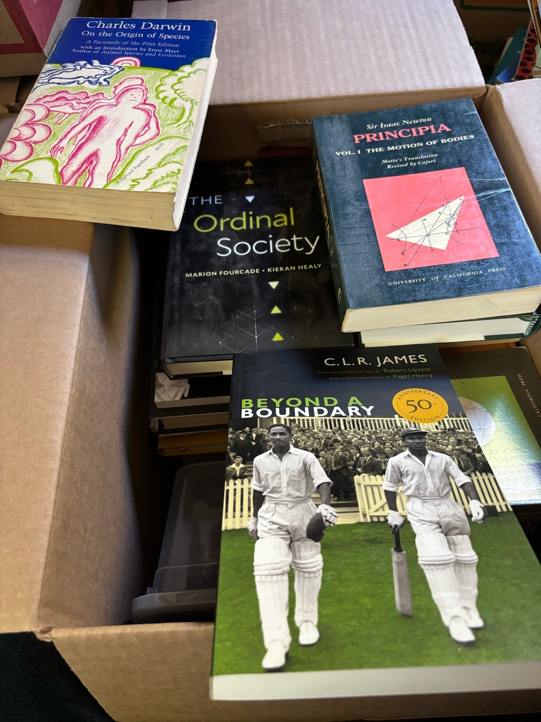 A box of books, with a few pulled out.  Visible covers include Newton's Principia (vol 1), Darwin's Origin of the species, CLR James' Beyond a Boundary, and Kieran Healey and Marion Fourcade's The Ordinal Society