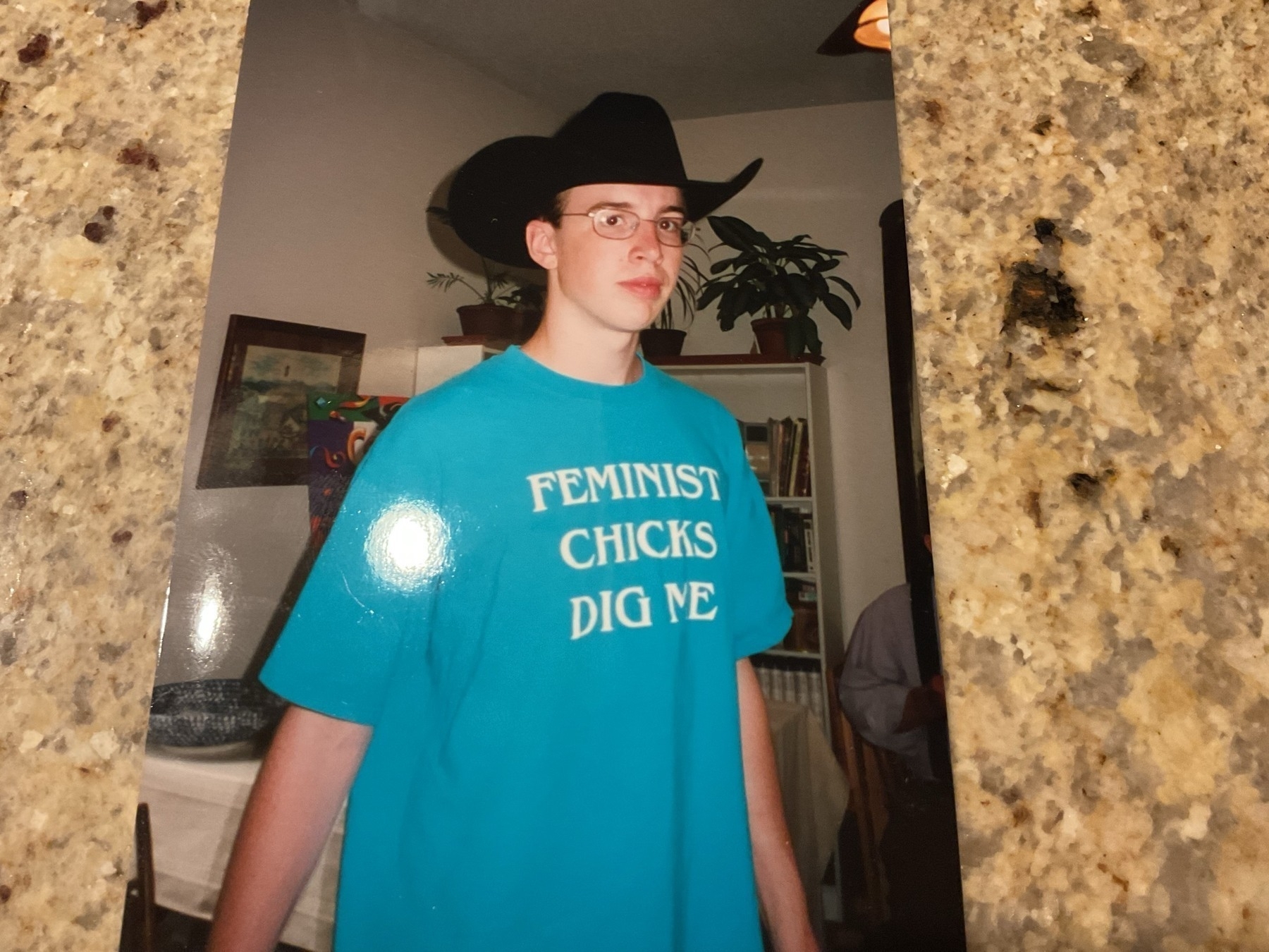 Photograph of a white teenager in a bright blue shirt with white letters reading "feminist chicks dig me" and a big black cowboy hat.