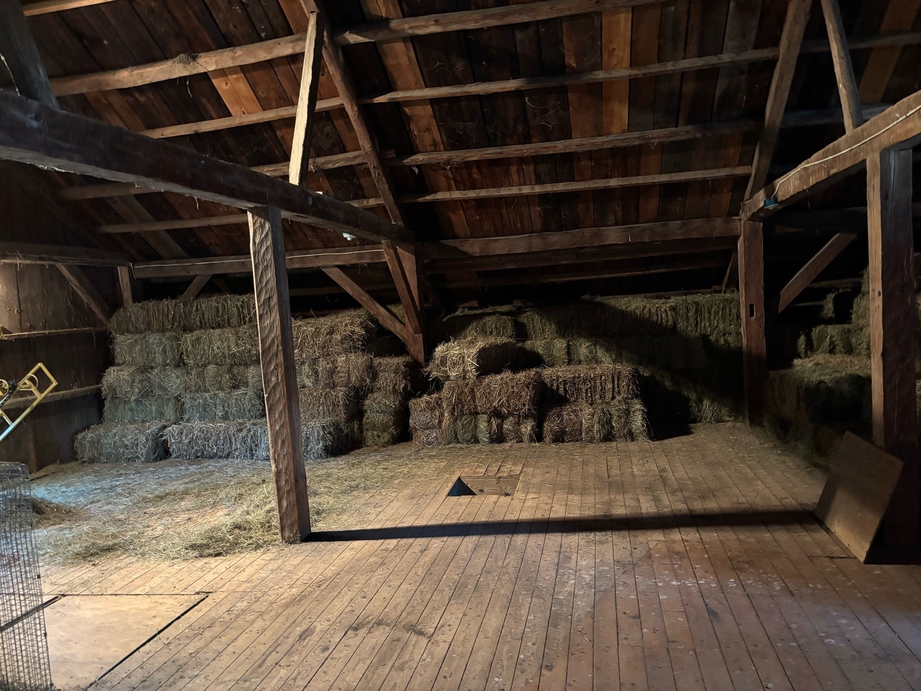 Another view of wooden frame barn with a row and a half of hay bales stacked although incompletely.