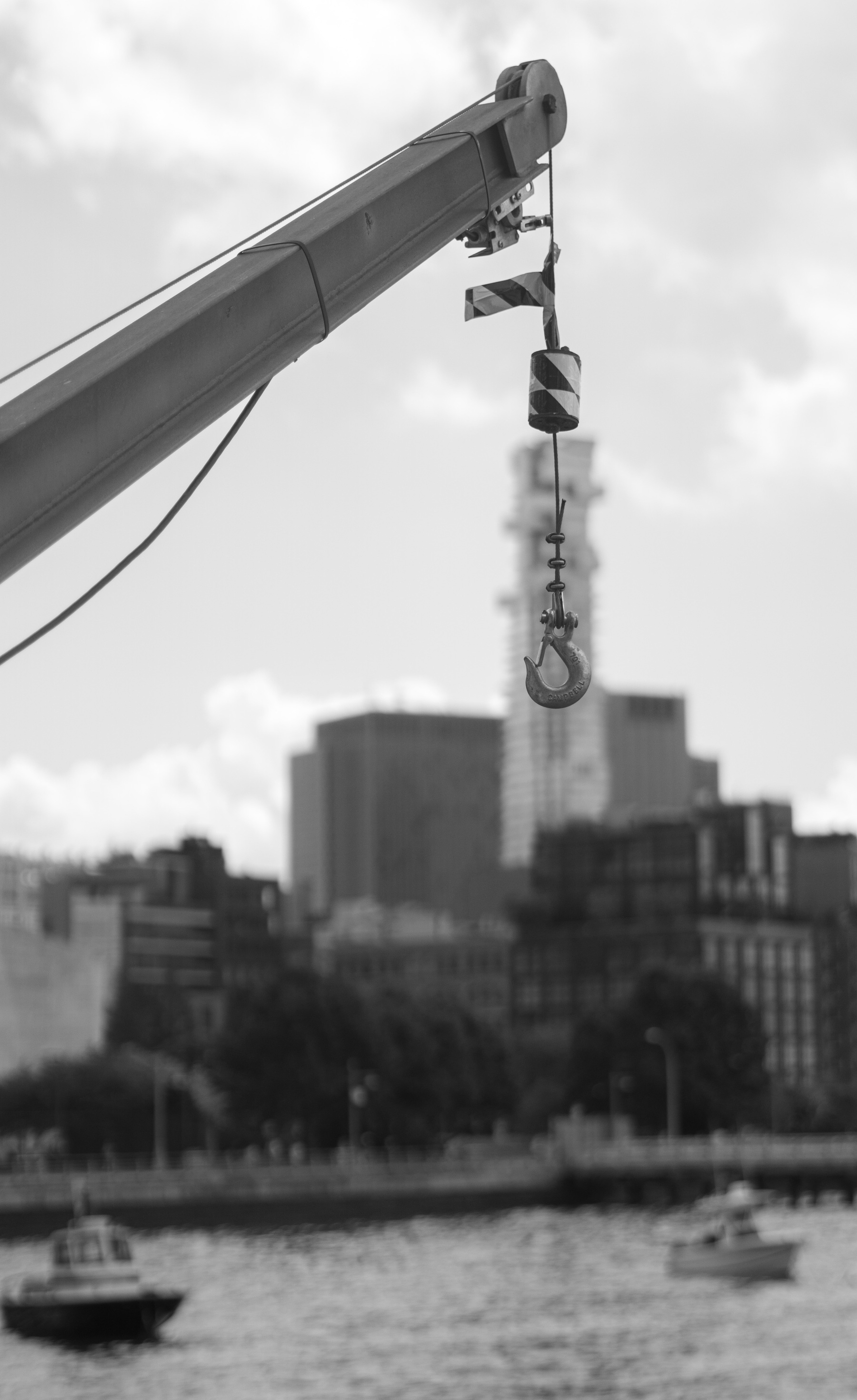 A hook lift with a hook in the foreground, the Hudson River with some of the city's skyline with two boats in the background.