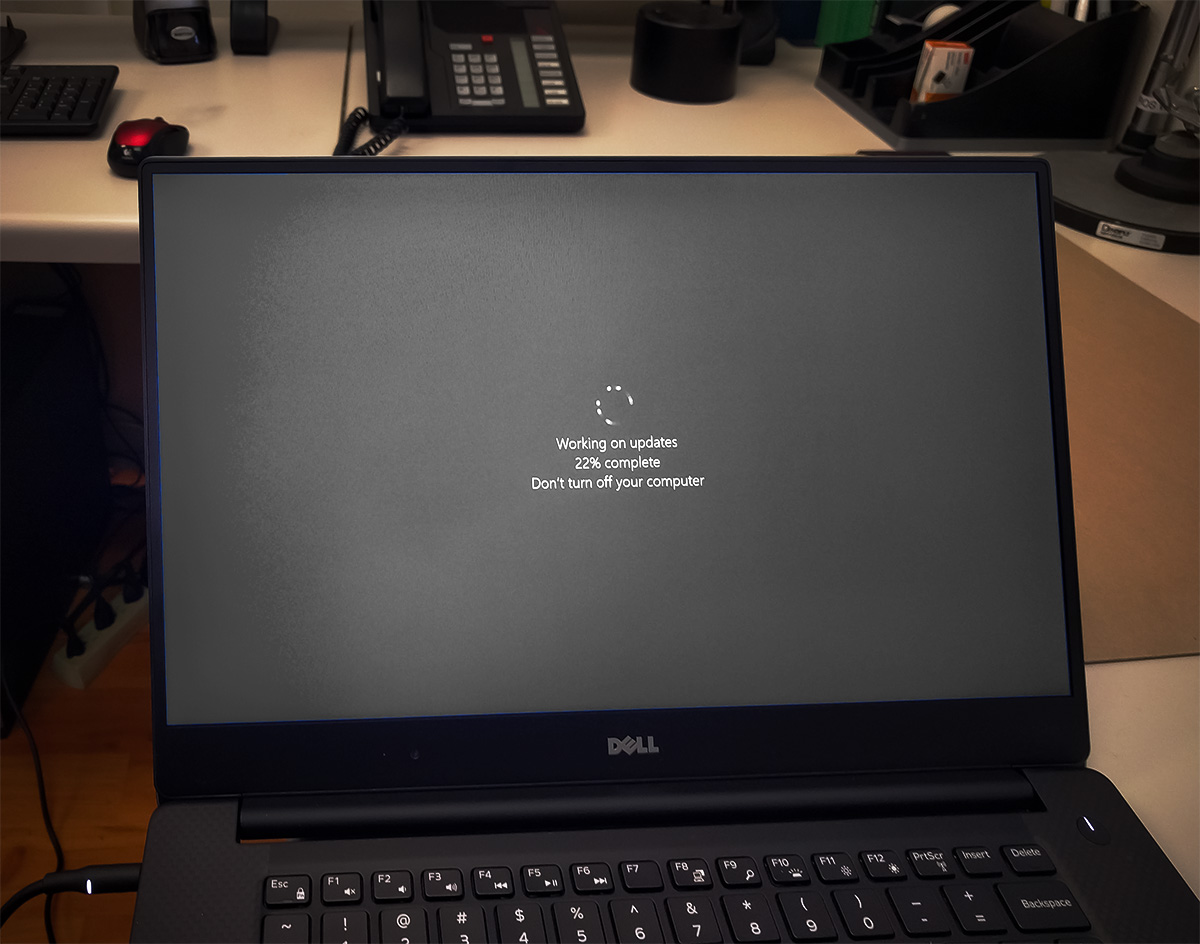 A 13-inch personal laptop displaying a 'Working on Updates' Microsoft Windows message. In the background, an office.