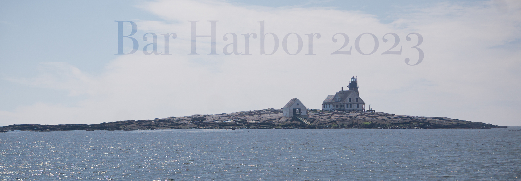 A picture of lighthouse island in Bar Harbor, Maine, from a deck on a boat. A text in the sky reads Bar Harbor 2023