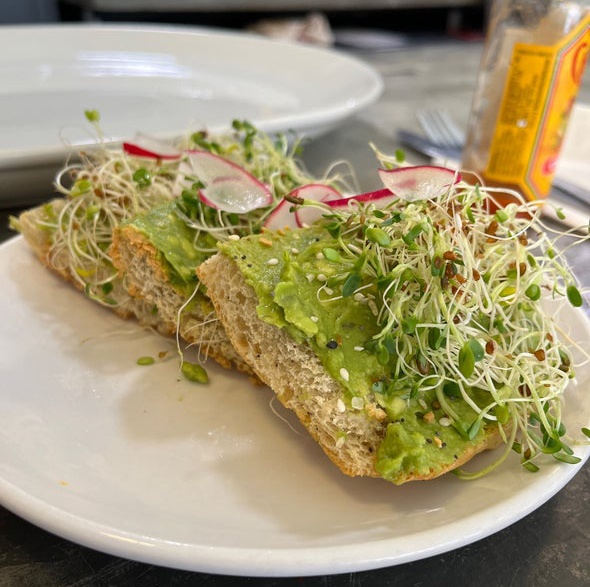 A three-slice Avocad toast with sprouts and reddish. Some hot suace is springled on top.