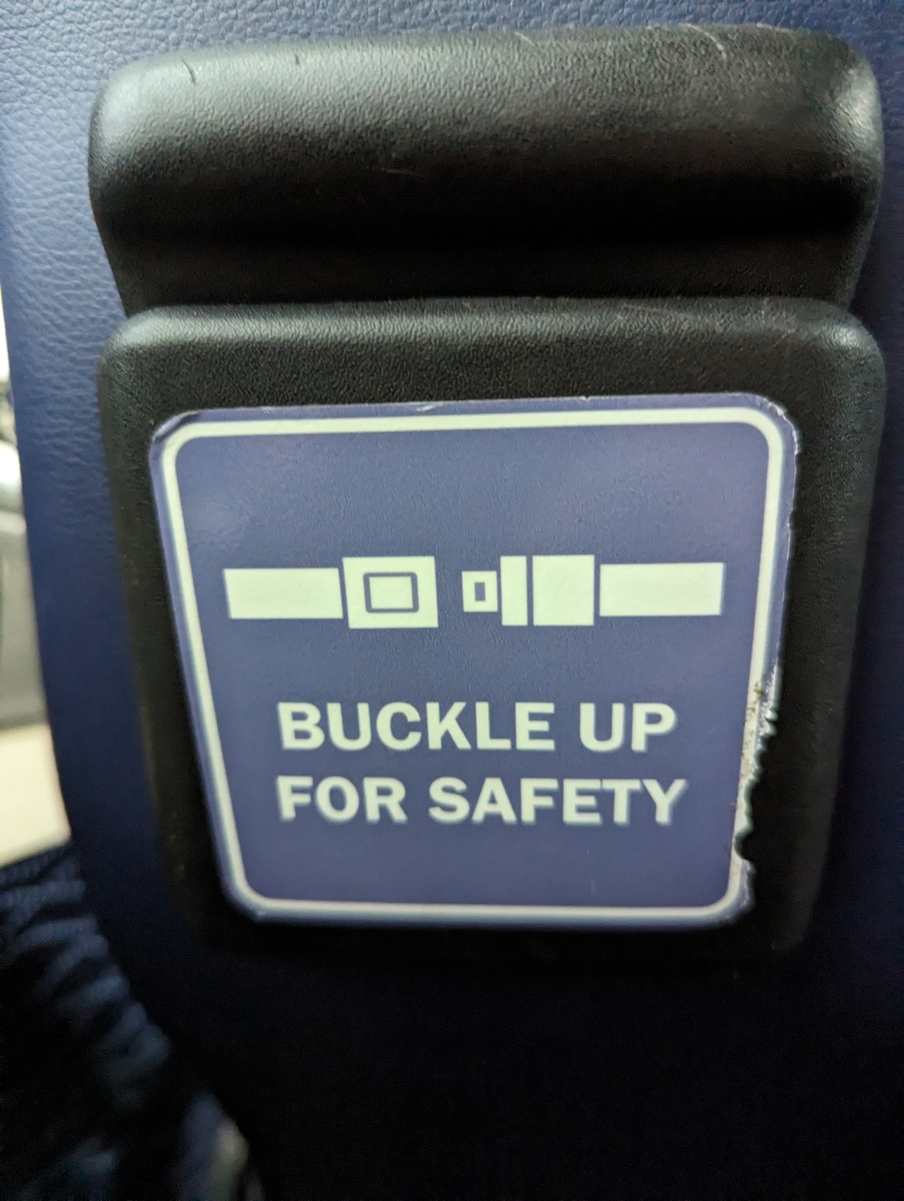 A sign on the back of a bus seat saying buckle up for safety