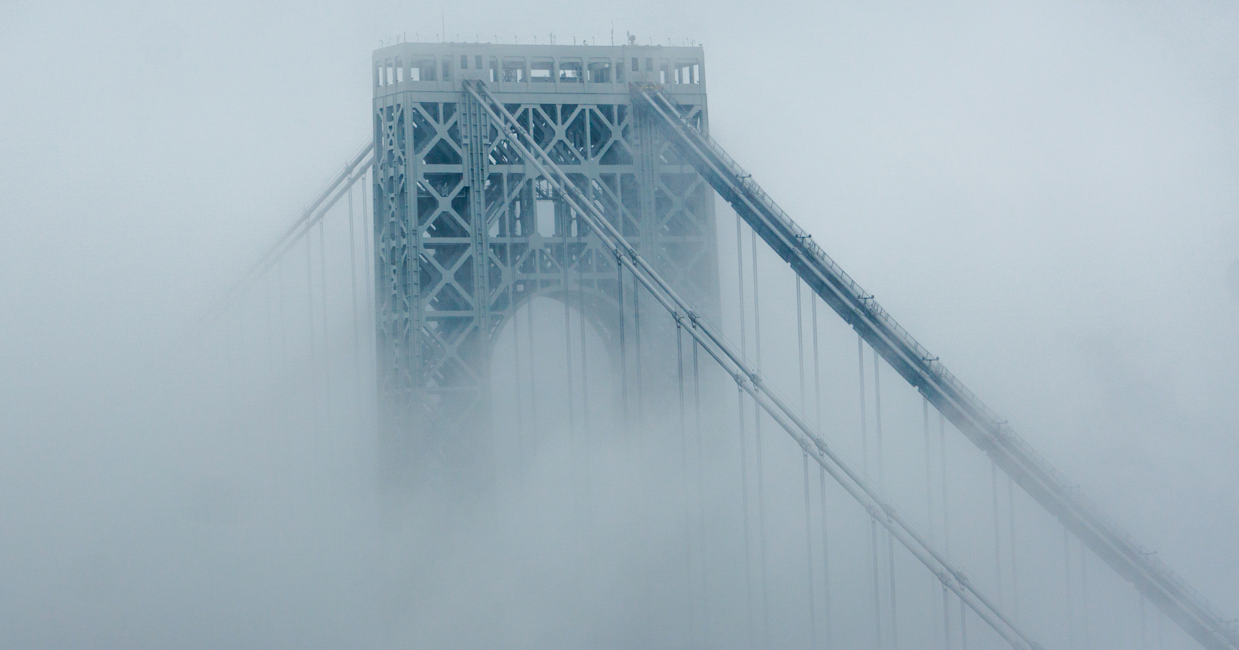A main pillar of a hanging bridge, the George Washington Bridge, immersed in the morning fog. Only the top shows, the rest is hidden behind the vapor