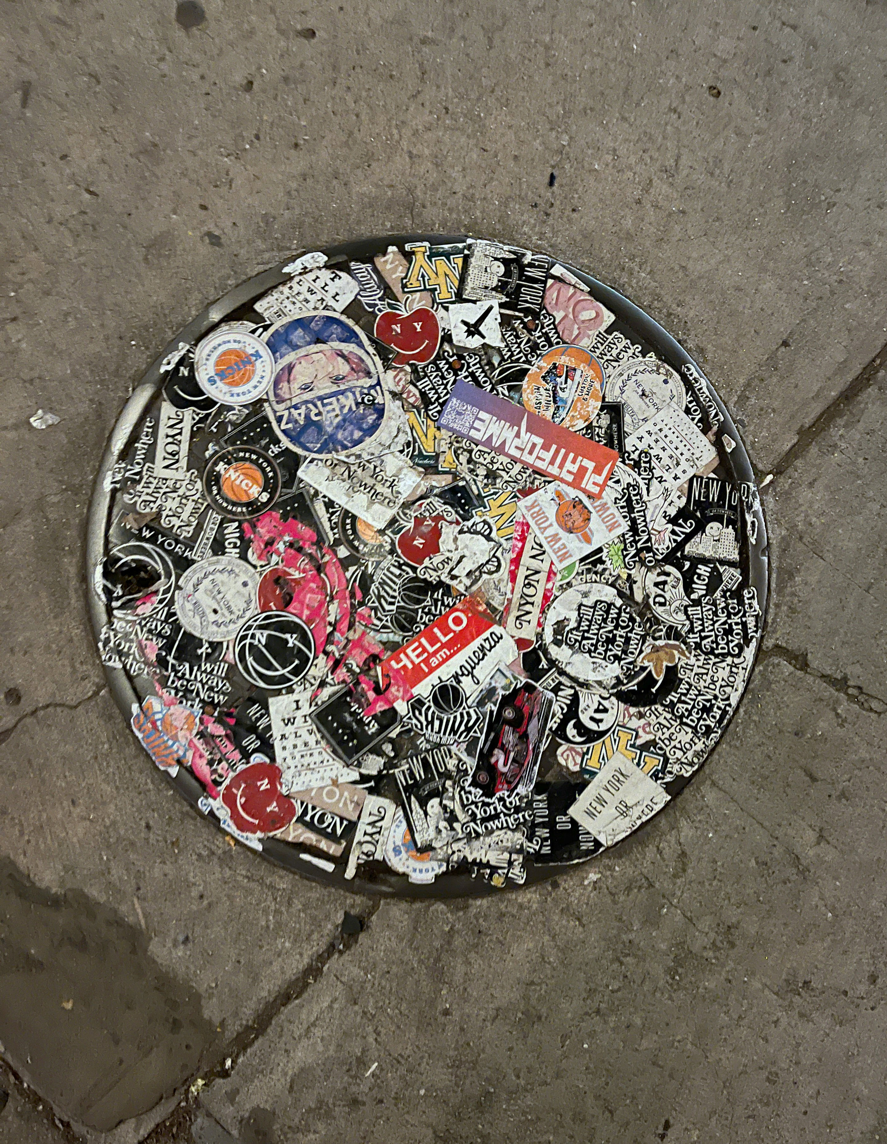 A manhole lid covered in various stickers, mostly look like graffiti and various writings.