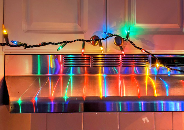 A range hood reflecting green, yellow, and blue lights from hanging small lightbulbs on a wire.