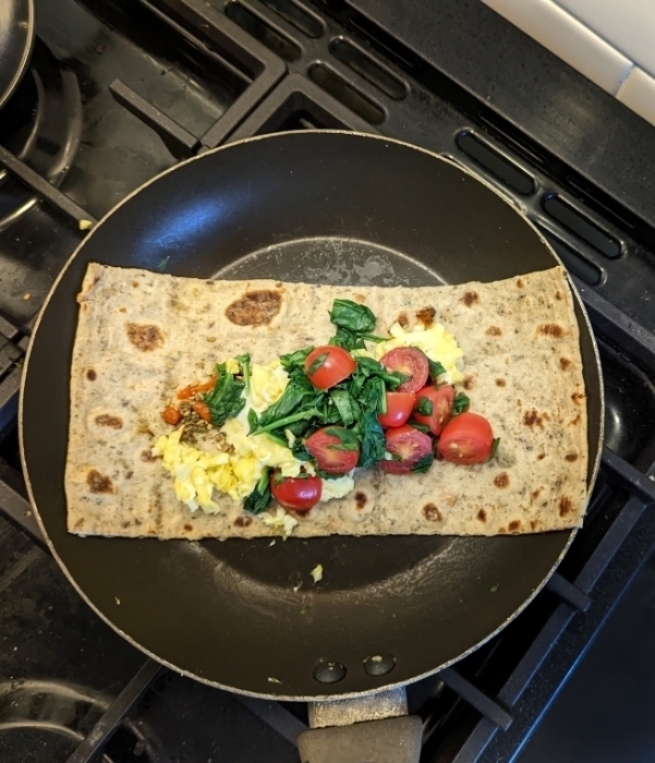 Auto-generated description: A flatbread in a pan is topped with scrambled eggs, spinach, and cherry tomatoes.