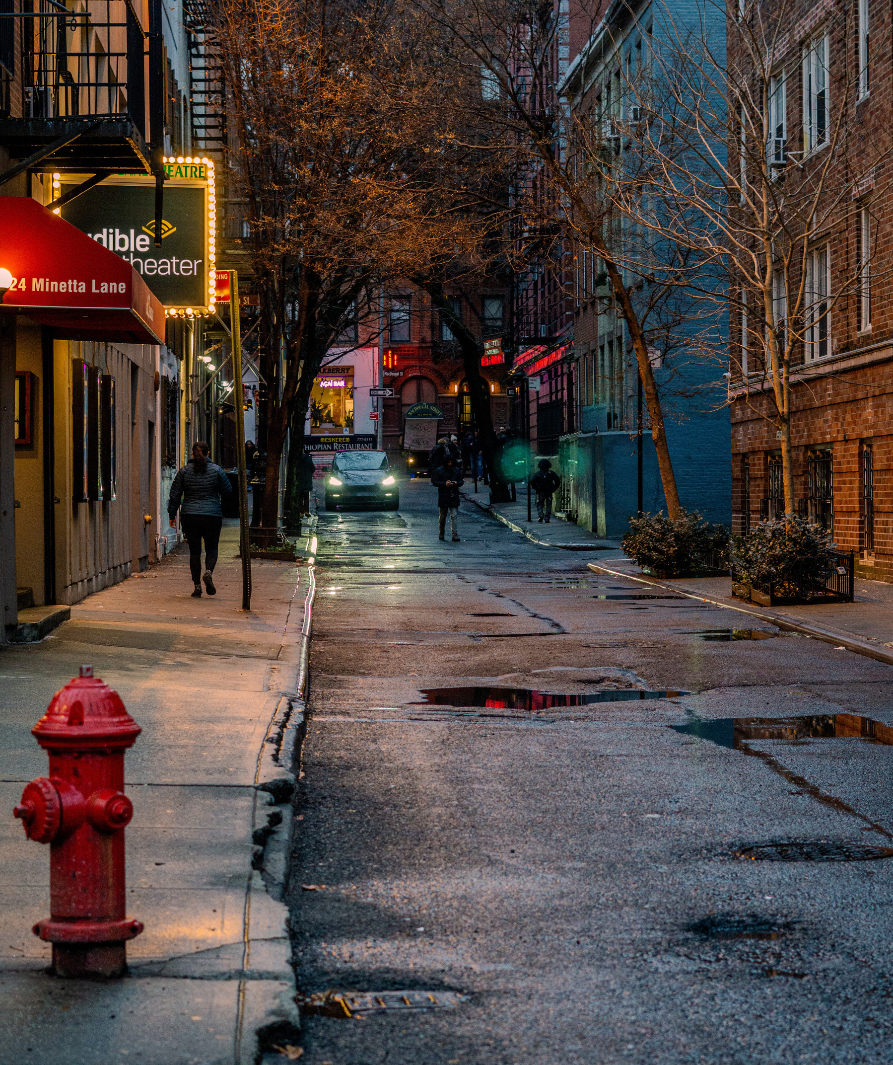 Minetta lane, off of 6th Ave. A red fire hydrant in the foreground, a street with puddles in the background, with lights from different shops further back