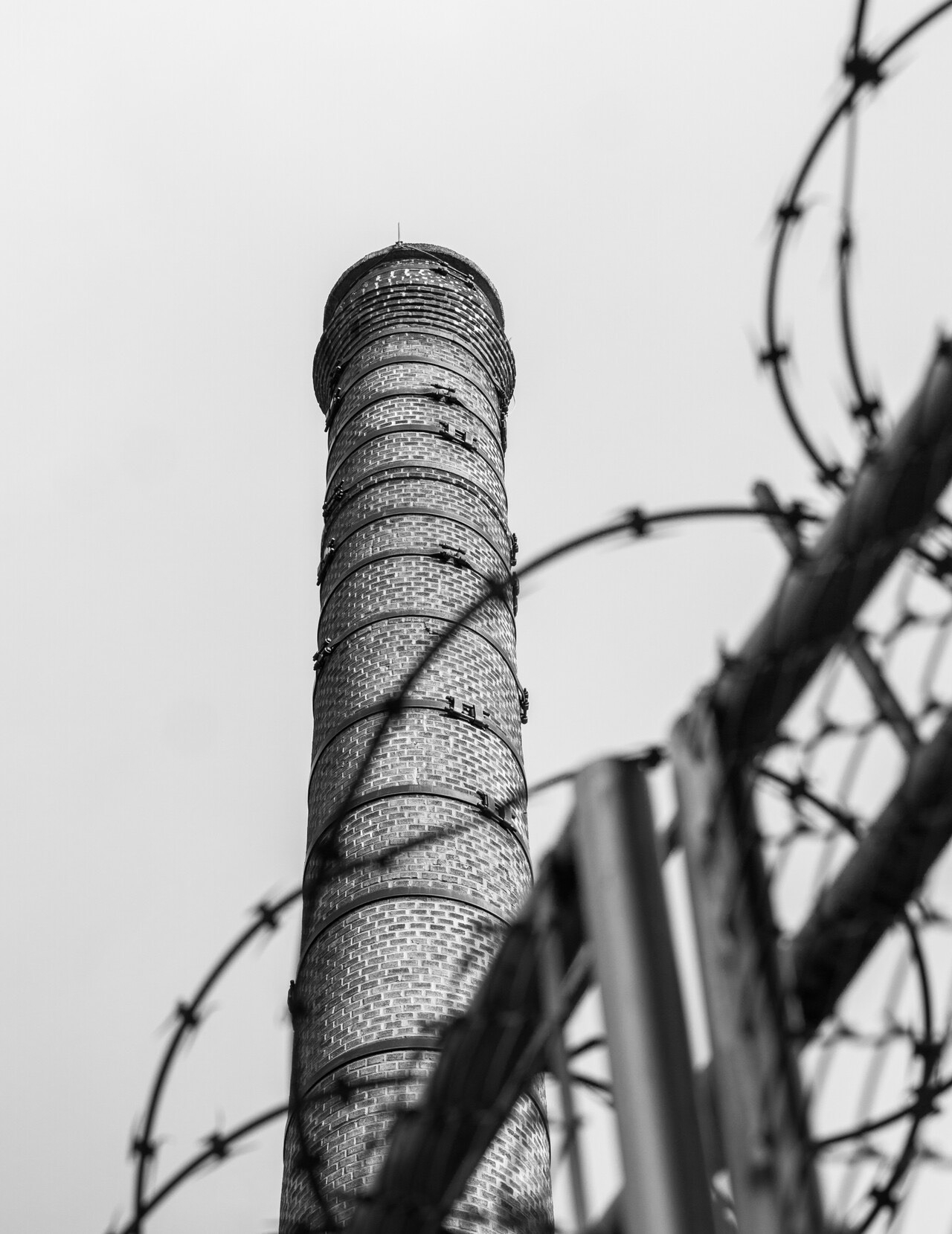 a black and white photo of smokestack behind barbed wire