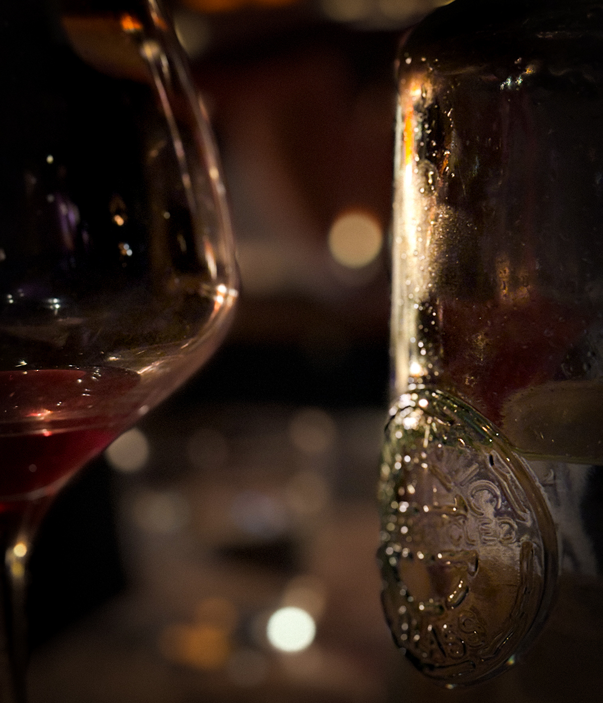 A close-up view showcasing a wine glass with red wine alongside a drink in a glass jar in a dimly lit room.