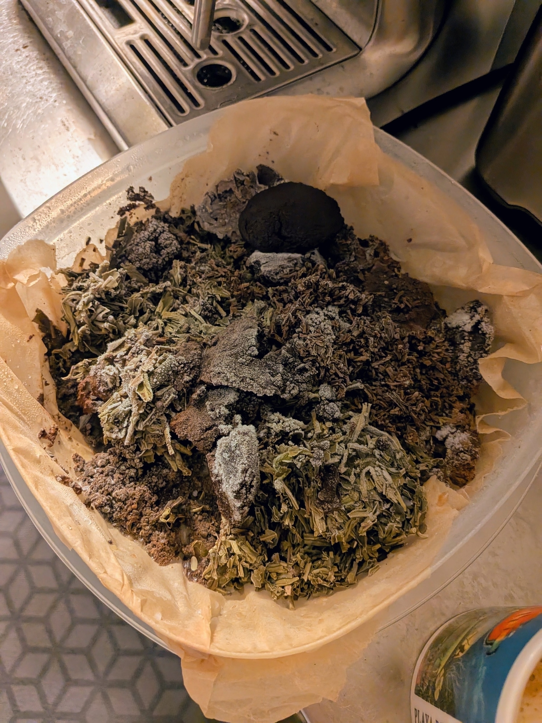 A container filled with coffee grounds and organic green and black tea is sitting on a counter.