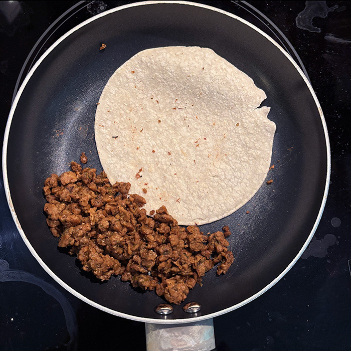 A tortilla and vegan ground meat (chorizo) are being prepared in a frying pan.