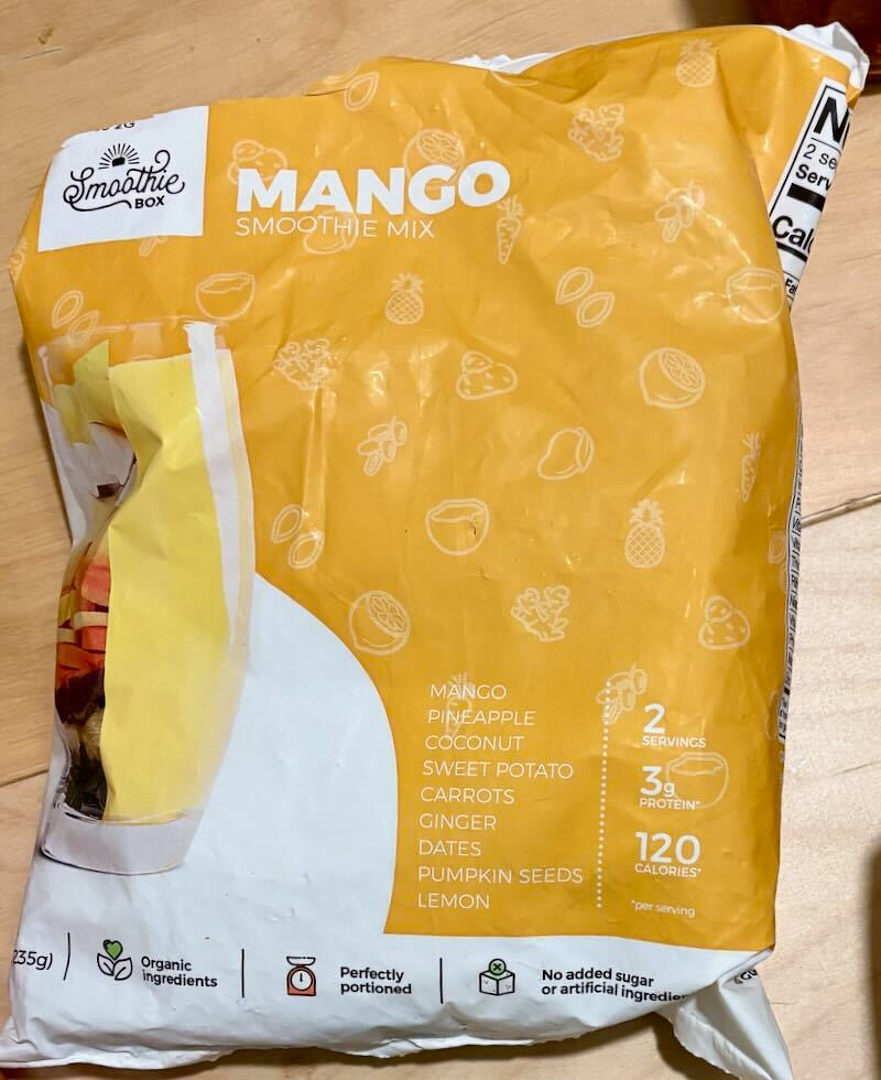 A bag of Mango Smoothie Mix from Smoothie Box is shown, featuring ingredients like mango, pineapple, and sweet potato, with nutritional details and organic certification.