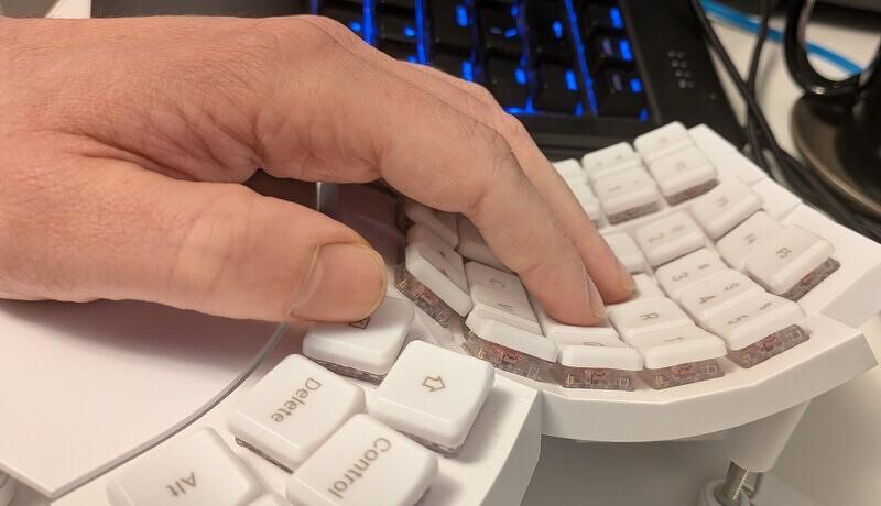 A hand is resting on keys that are curved downward on a keyboard with white keycaps.