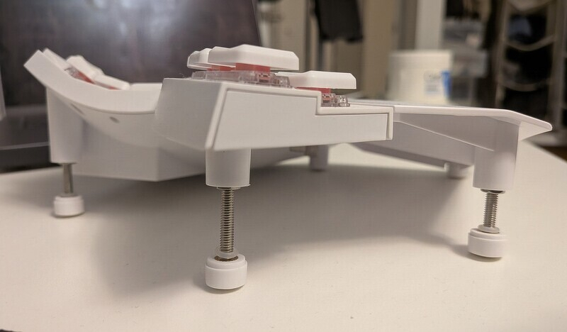 A close-up view of a white keyboard with adjustable screw legs.