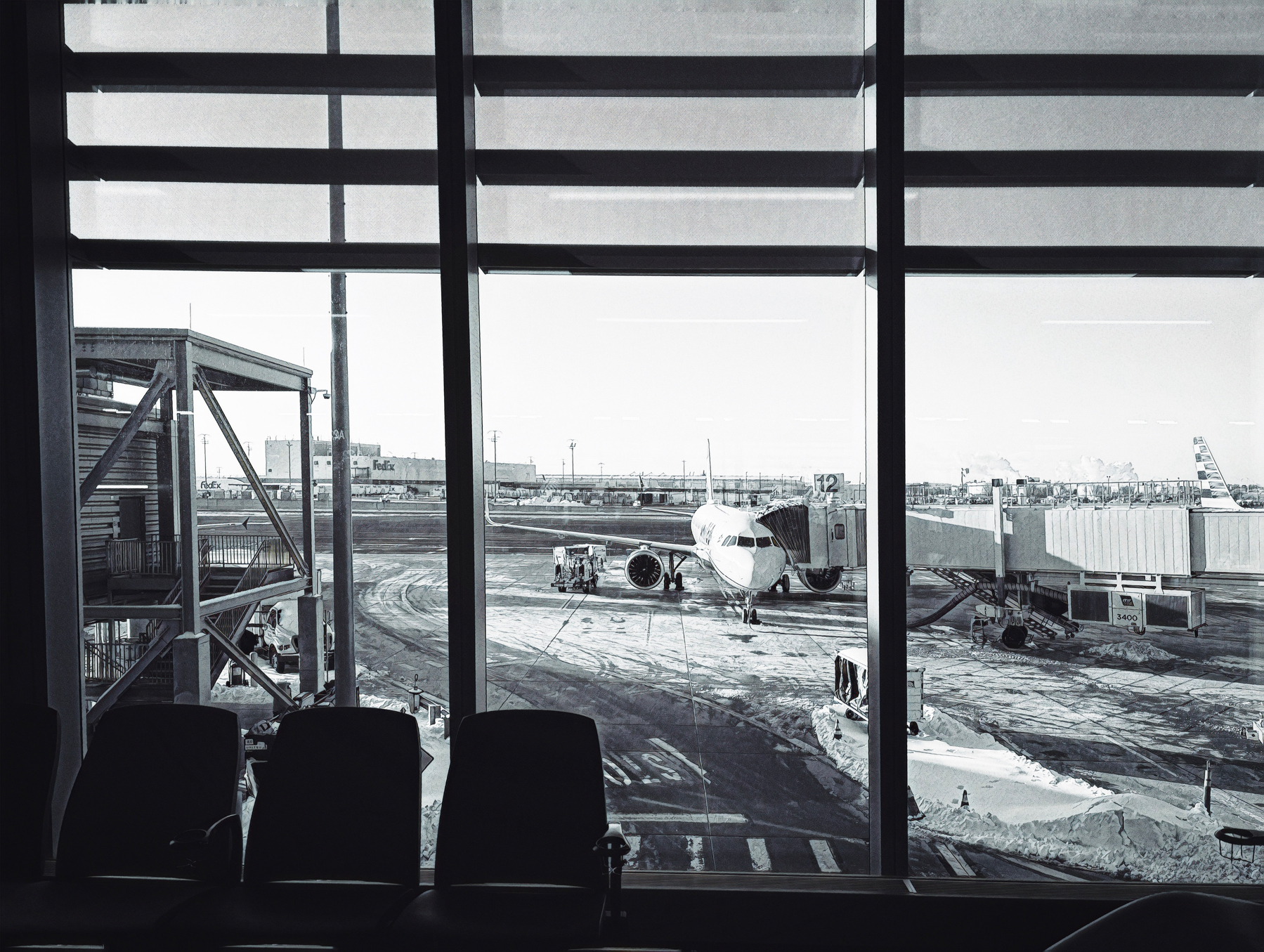 A parked airplane is visible through large windows at an airport terminal with empty seats in the foreground.
