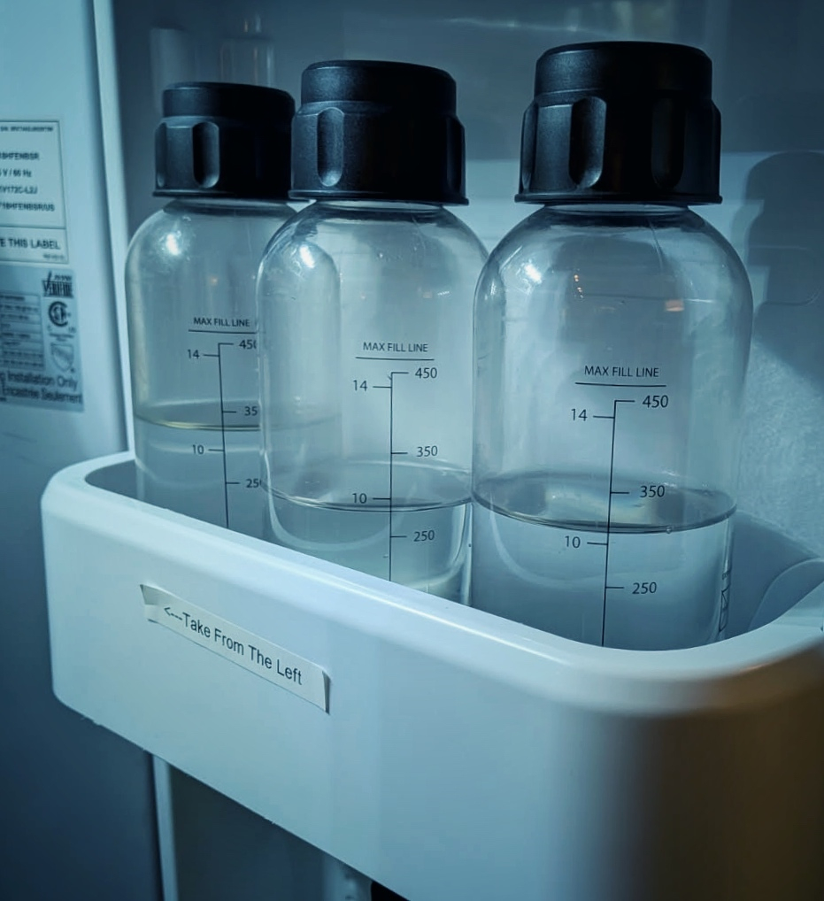 Three transparent bottles filled with sparkling water are lined up in a refrigerator door compartment.