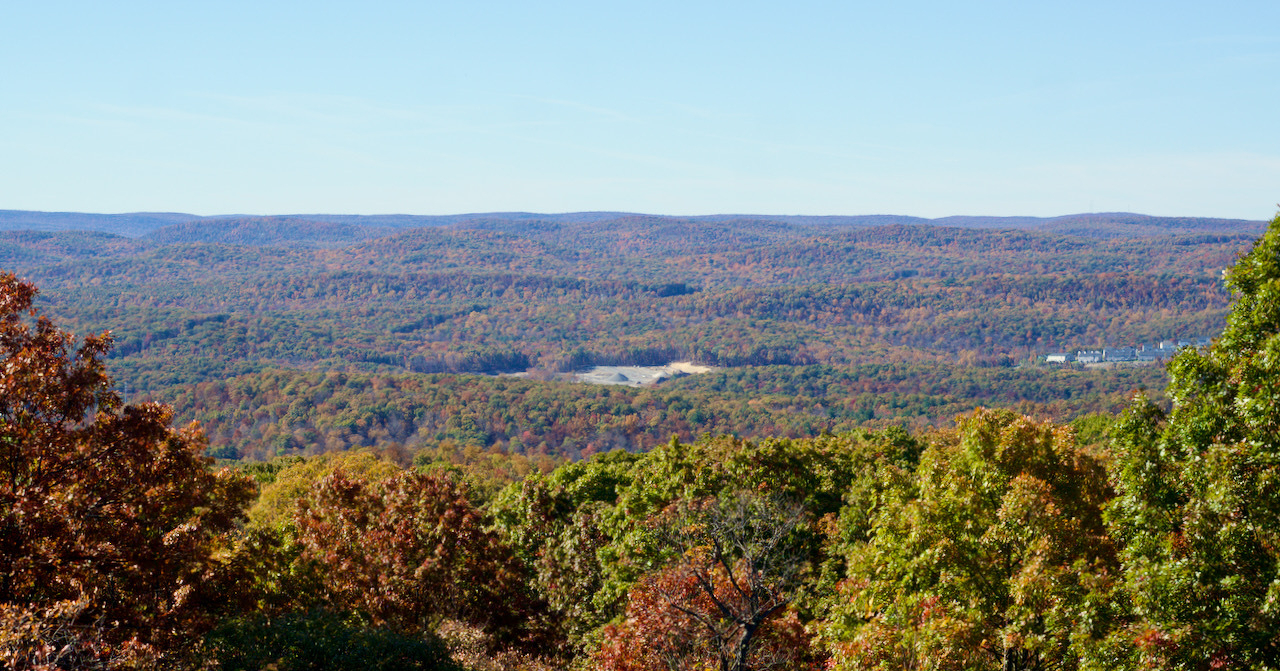 Auto-generated description: A vast landscape of rolling hills covered in autumn-colored trees stretches under a clear blue sky.