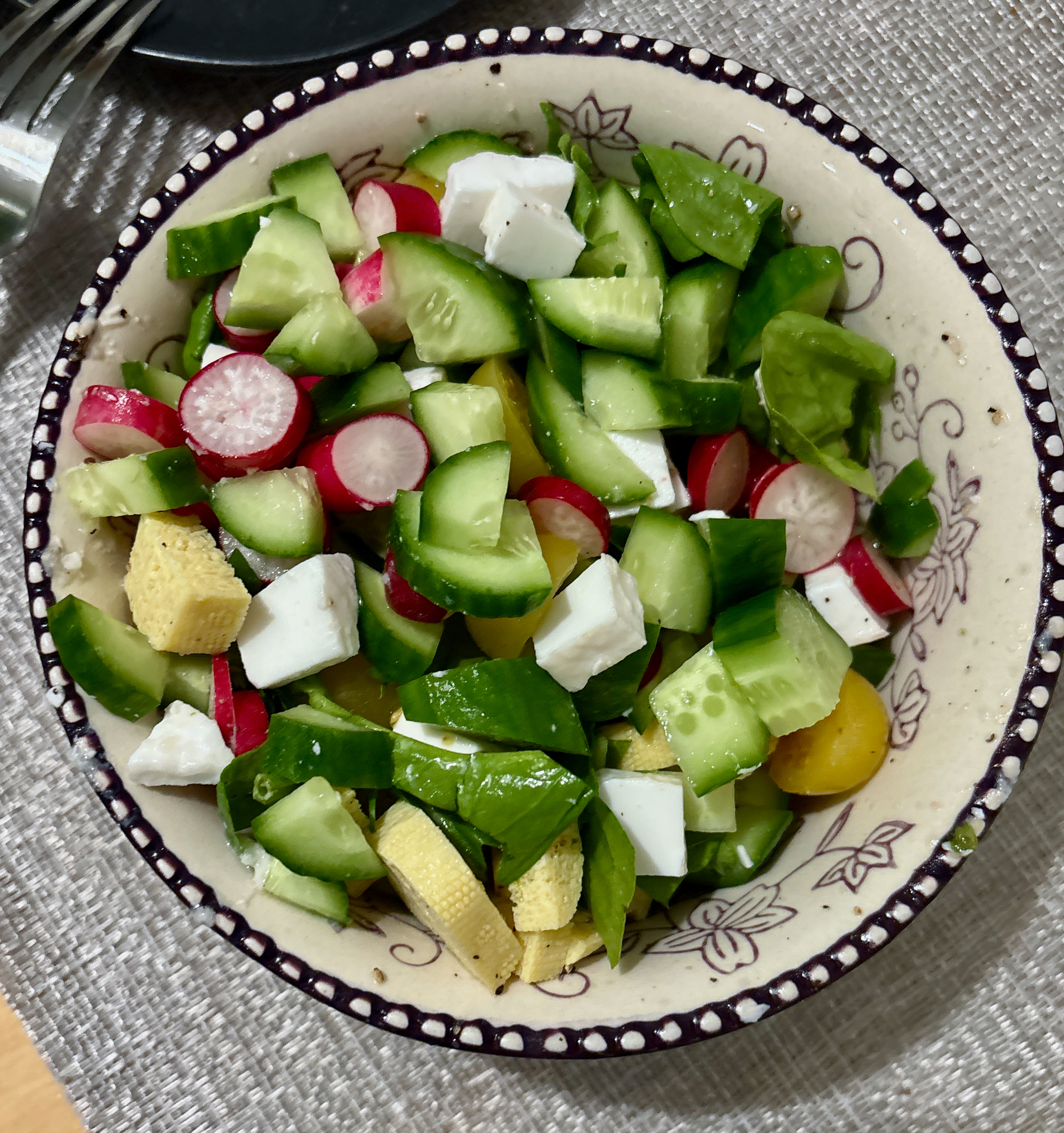 A vibrant salad features chopped cucumbers, radishes, vegan cheese, tufo, and other fresh vegetables in a bowl.
