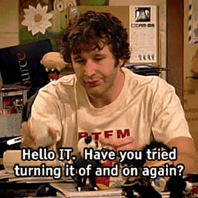 Auto-generated description: A man is sitting in a cluttered office and asking, Hello IT. Have you tried turning it off and on again?