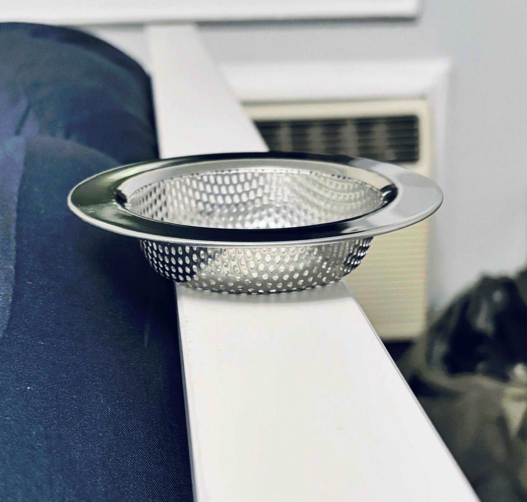 A metallic mesh sink strainer is placed on the edge of a white surface