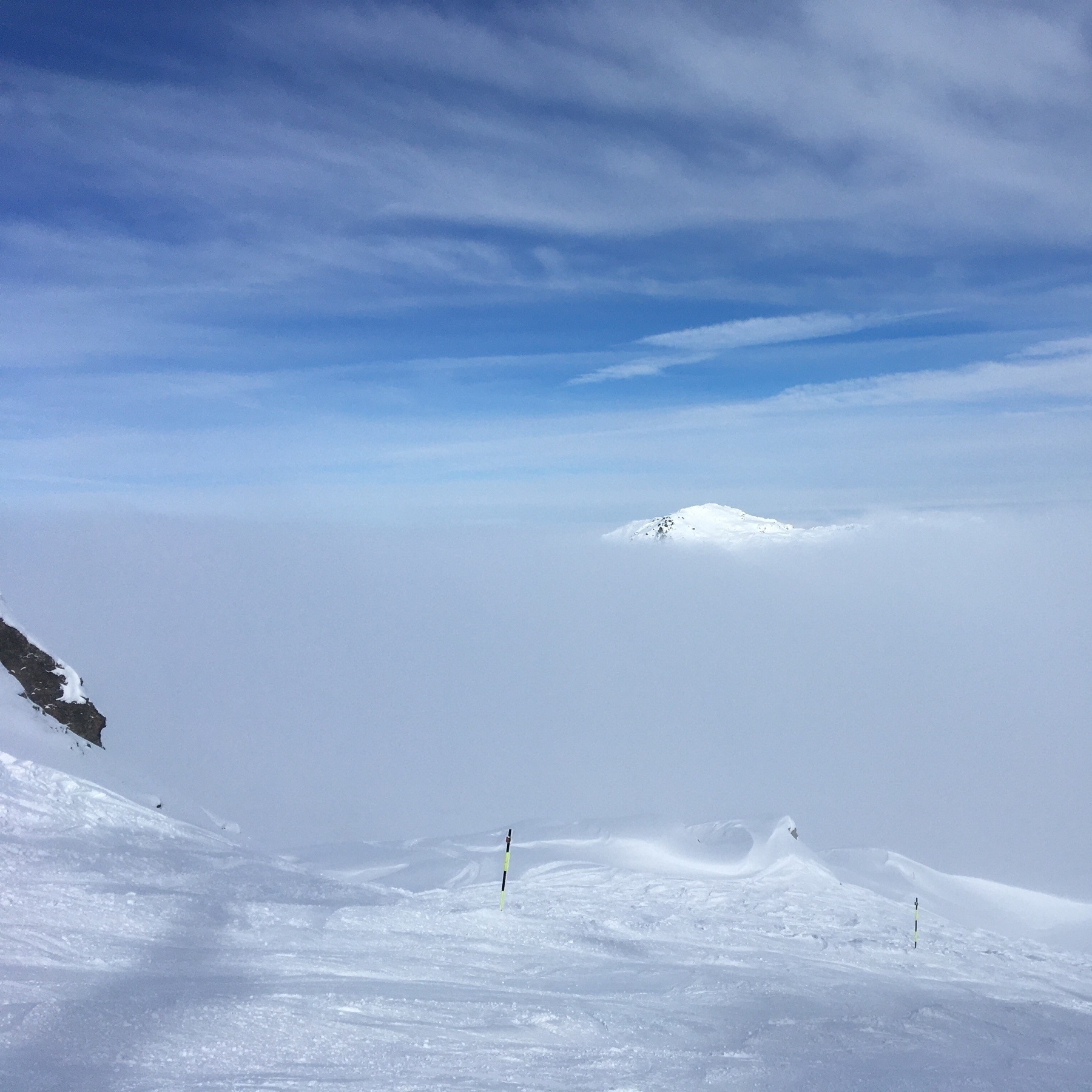 Snowy mountain peak peeking out of a layer of cloud. Ski slope in the foreground.