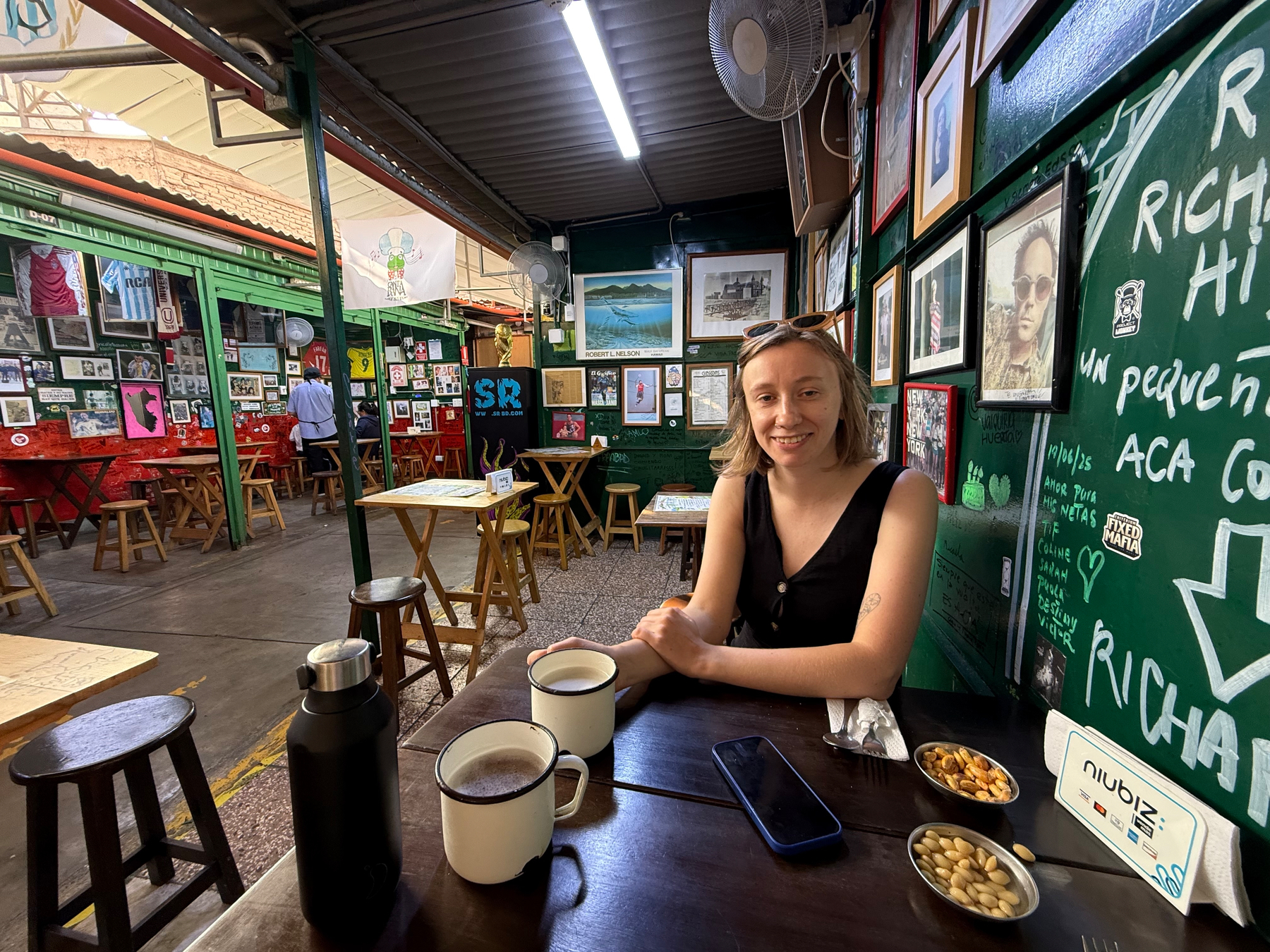 A person is sitting at a table with drinks and snacks in a colorful, art-filled café.