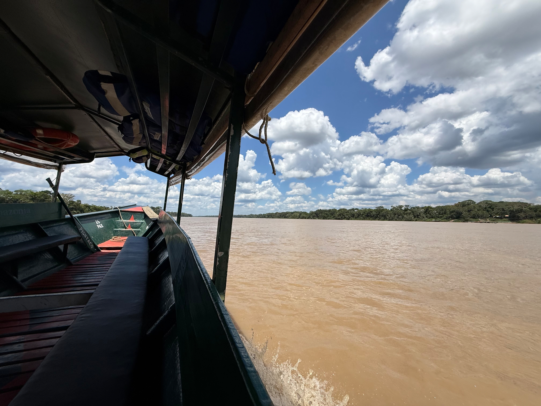 A boat is navigating along a wide, muddy river under a sky filled with fluffy clouds.