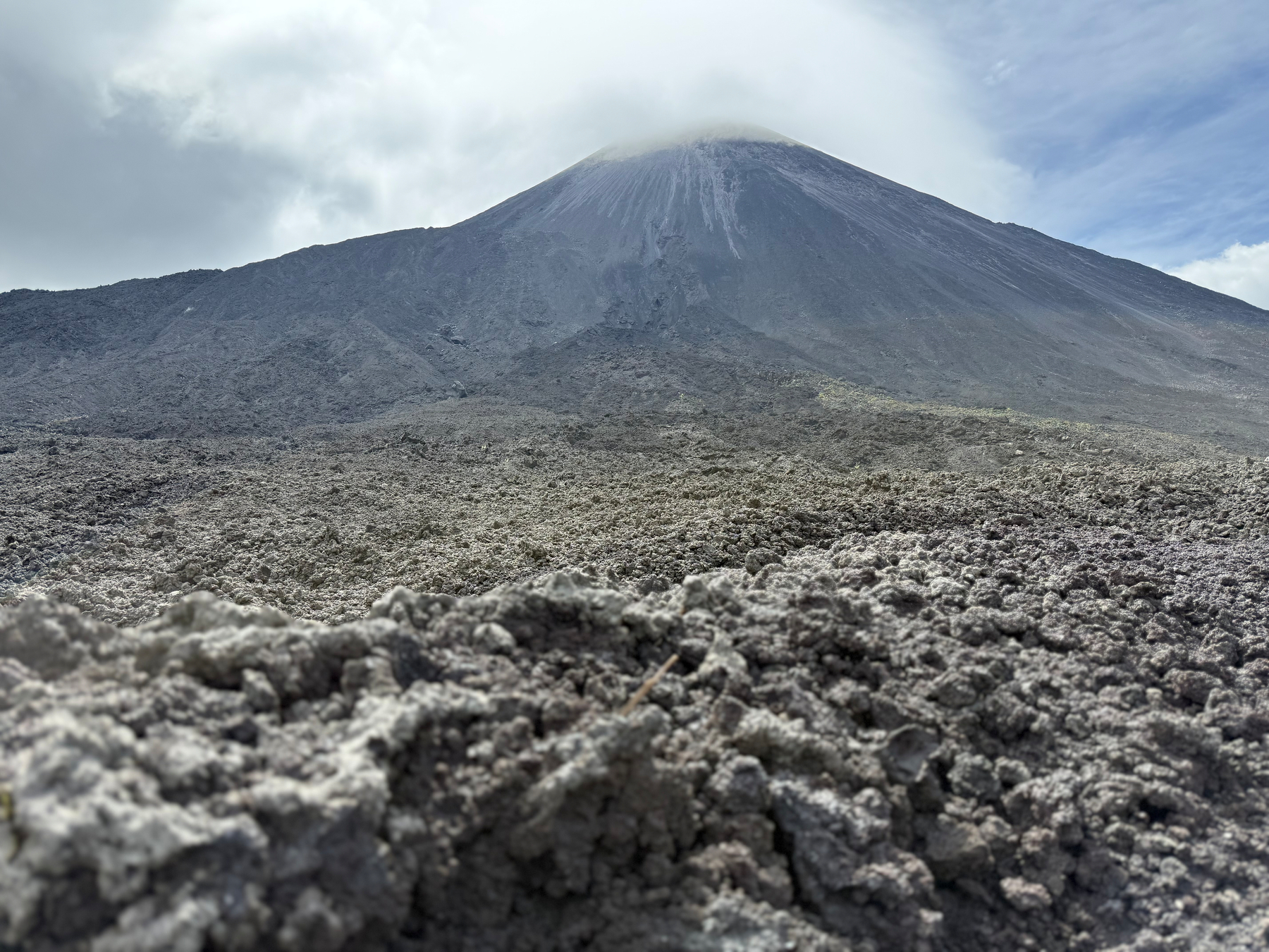 Auto-generated description: A volcanic landscape features a rugged, rocky terrain with a cloud-covered mountain peak in the background.
