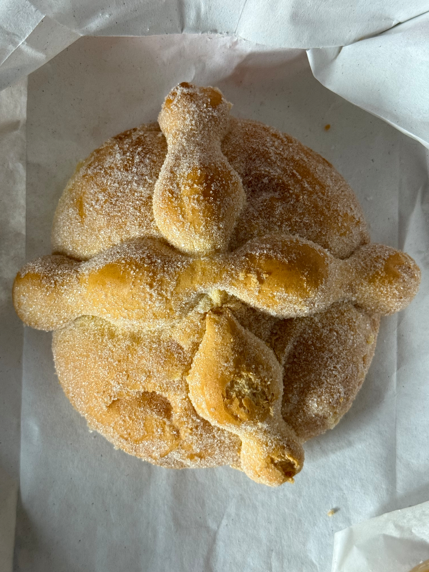 Auto-generated description: A round, sugar-dusted bread with bone-shaped decorations on top, likely a pan de muerto.