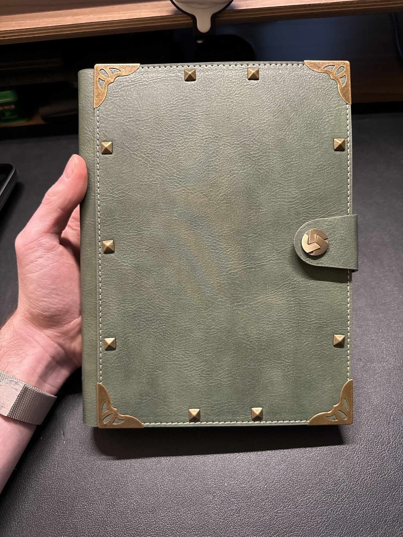 Image of a faux-leather-bound six-ring binder with bronze corner protectors and a button clasp. 