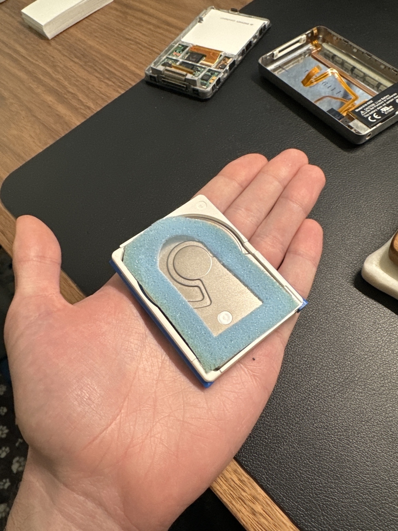 A photo of an 80 gb hard drive small enough to fit in the (admittedly large) palm of my hand. A partially disassembled 5.5th generation iPod sits on the desk in the background. 
